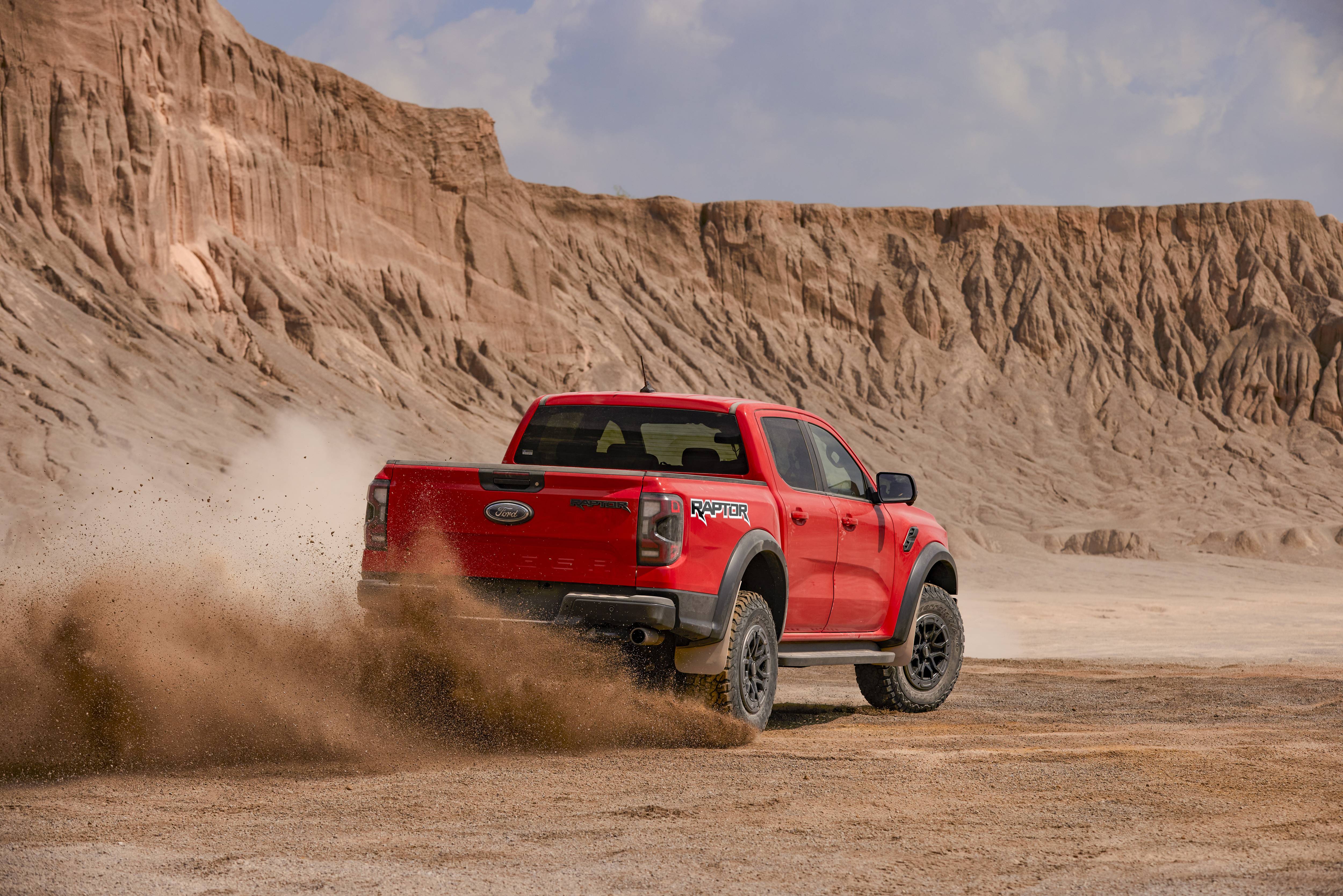 Red Ford Ranger Raptor kicking up dust driving off in clay like desert